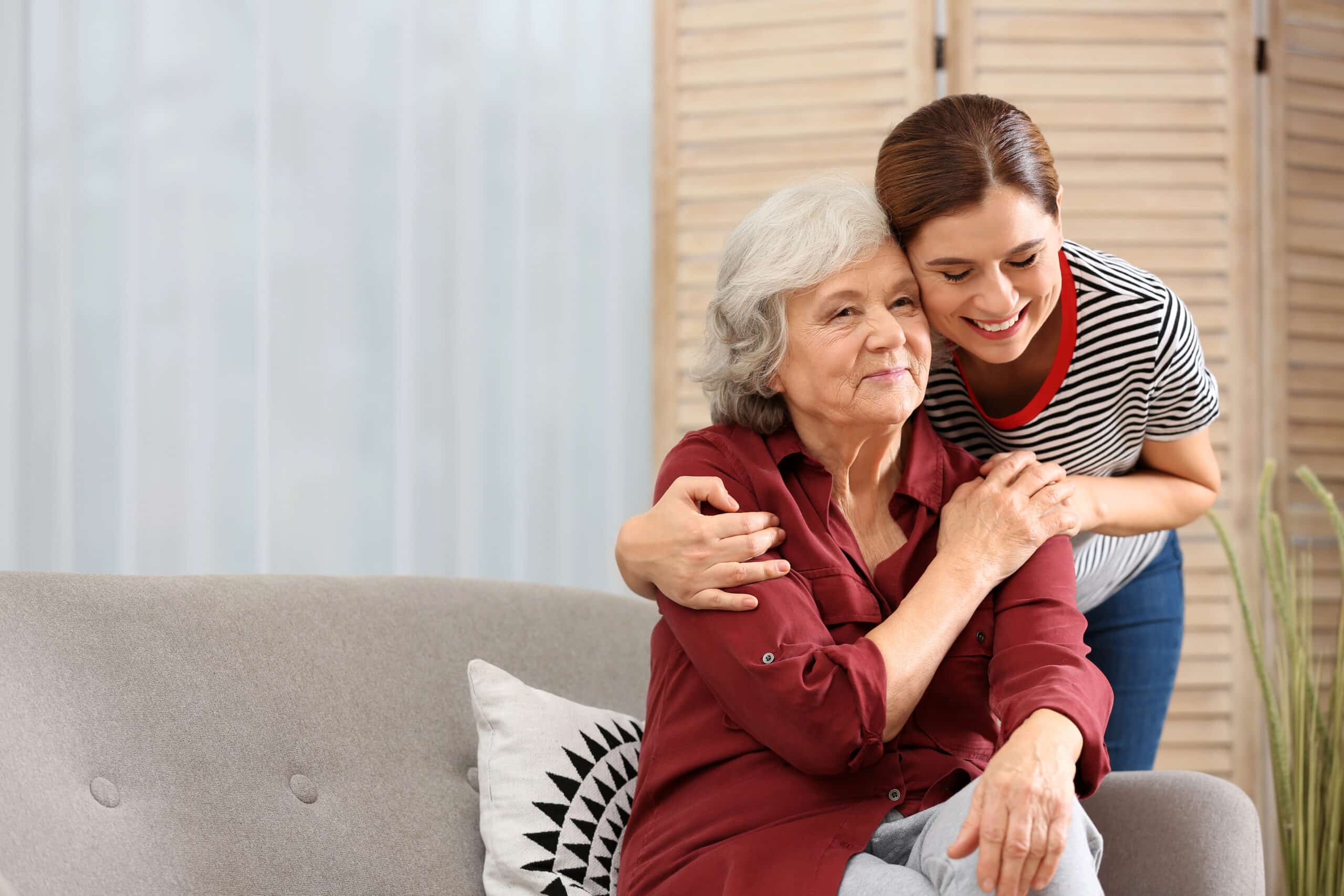 Elderly woman with female caregiver in living room. Space for text